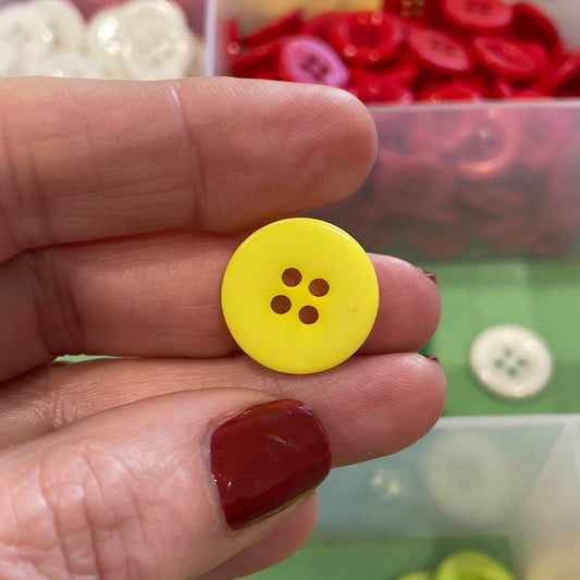Hand holding a yellow button with a colorful button collection in the background