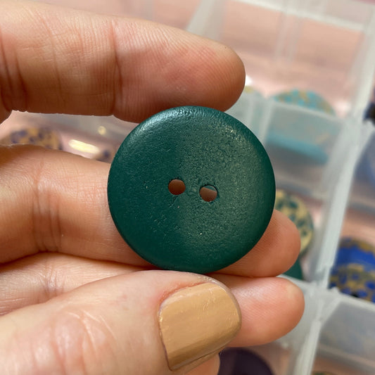 Hand holding a green button with a container of buttons in the background