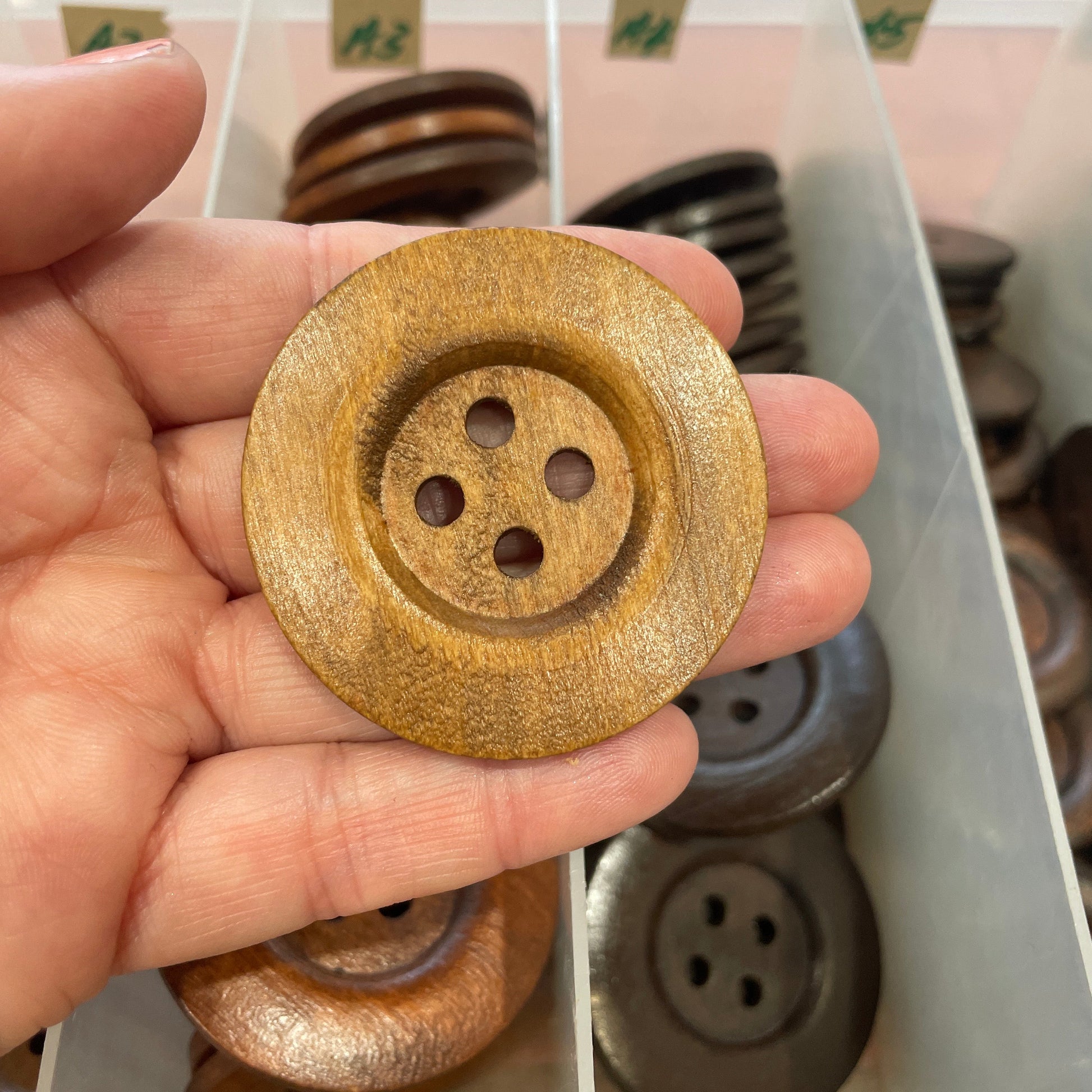 Gold button held in hand with a container of buttons in the background