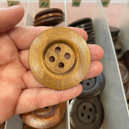 Gold button held in hand with a container of buttons in the background