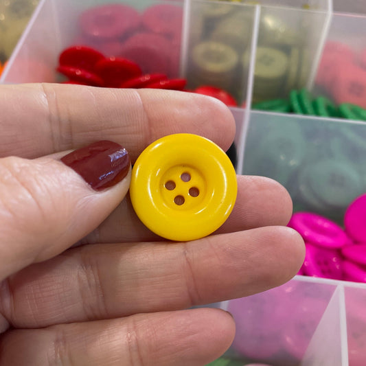 Hand holding a yellow button with a colorful button organizer in the background