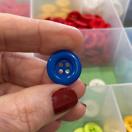 Hand holding a blue button with a transparent container of assorted buttons in the background