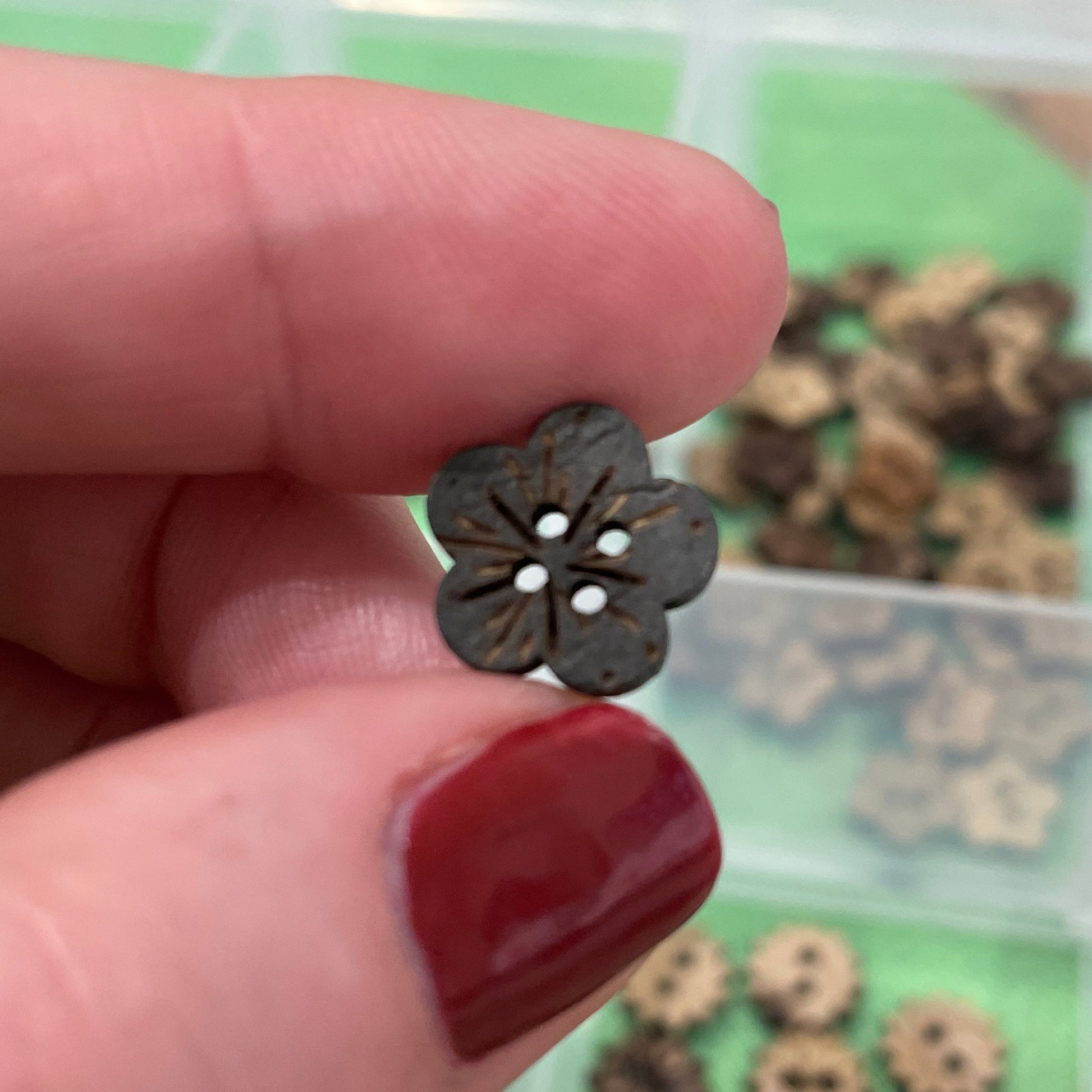 Hand holding a small flower-shaped button with a blurred background of buttons.