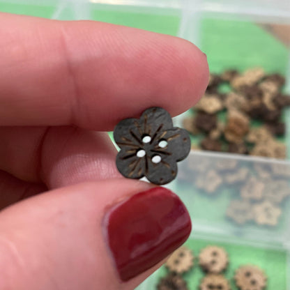 Hand holding a small flower-shaped button with a blurred background of buttons.