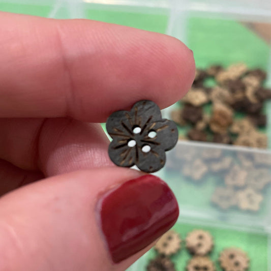Hand holding a small flower-shaped button with a blurred background of buttons.
