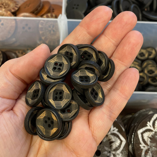 Hand holding black buttons with gold accents in front of a container of buttons.