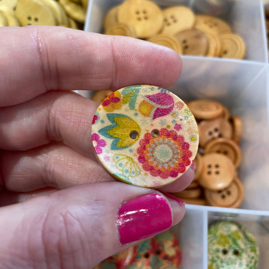 Hand holding a decorative button with a colorful design, surrounded by various buttons in the background.