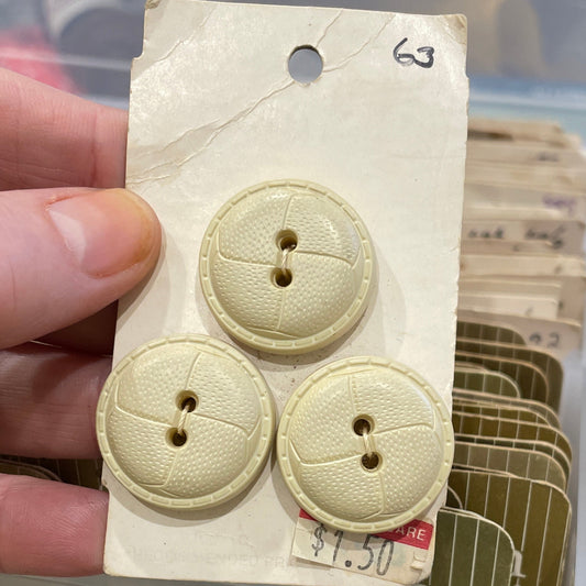Hand holding a card with three beige buttons in front of a container.