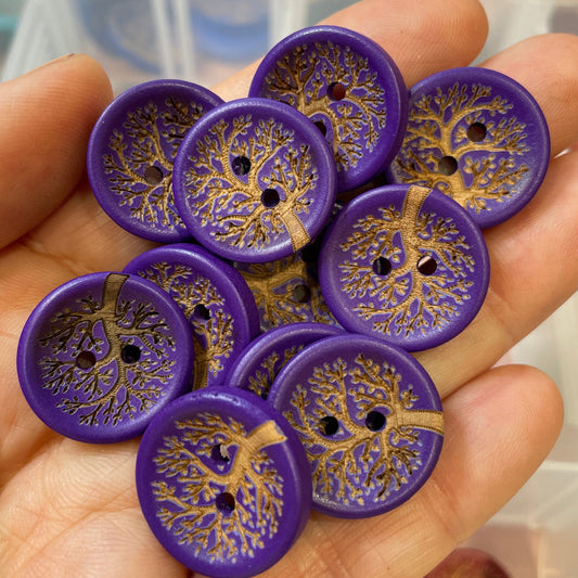 Hand holding purple buttons with tree design against a blurred background