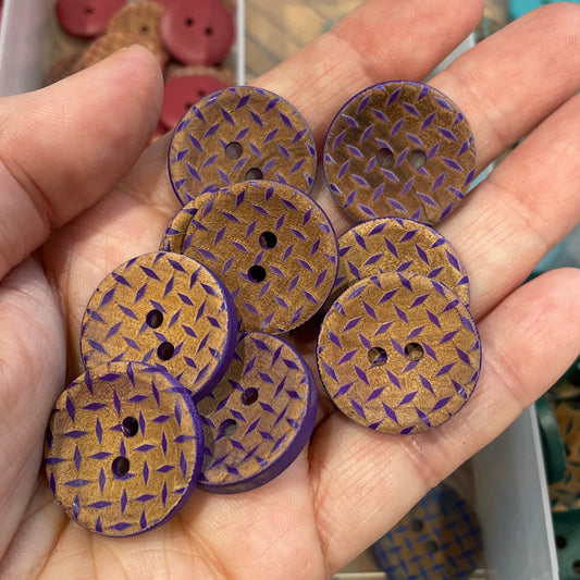 Hand holding purple and brown buttons with a container of buttons in the background