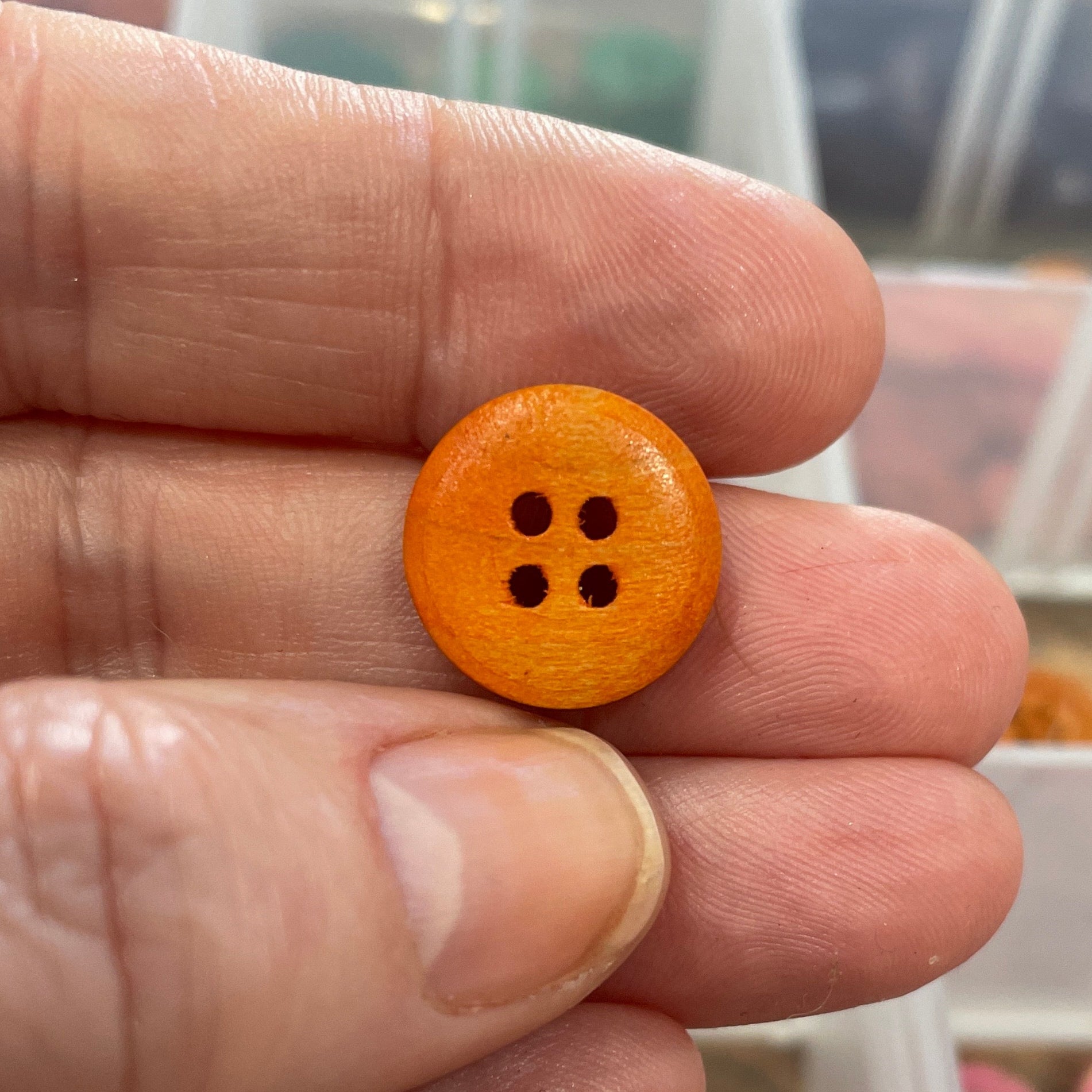 Hand holding a small orange button with a clear container of buttons in the background