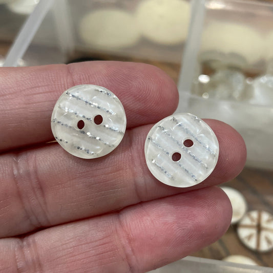Two white buttons held between fingers with a clear container of buttons in the background.