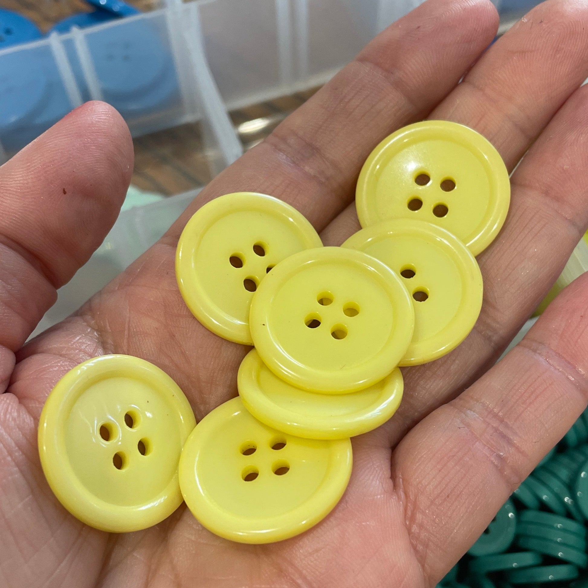 Hand holding yellow buttons with a container of assorted buttons in the background