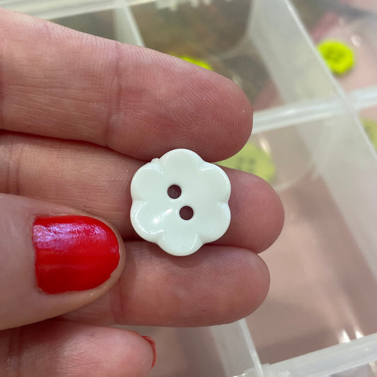Hand holding a white flower-shaped button with a blurred background of a container with buttons.