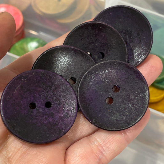 Hand holding black buttons with a background of assorted colored buttons.