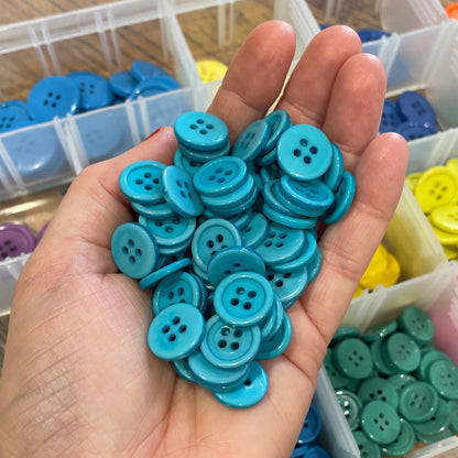 Hand holding blue buttons with a container of assorted buttons in the background