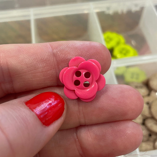 Pink flower-shaped button on a finger with a blurred background of buttons