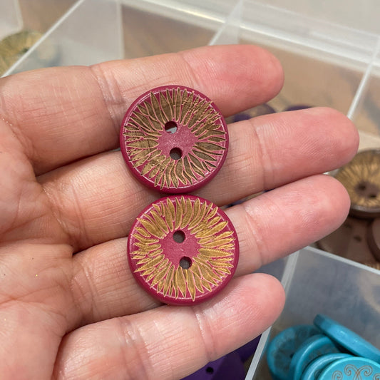 Hand holding two pink buttons with a container of various buttons in the background