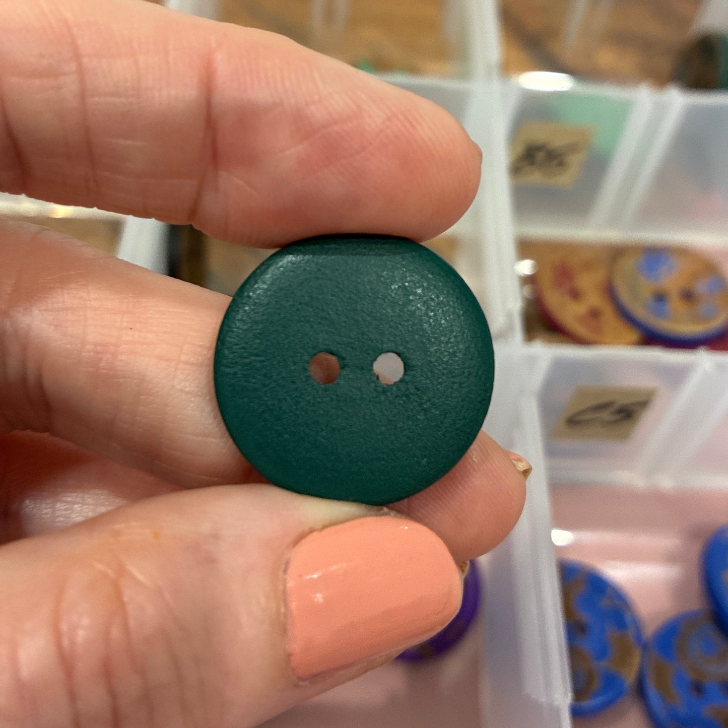 Hand holding a green button with a blurred background of a container with buttons.