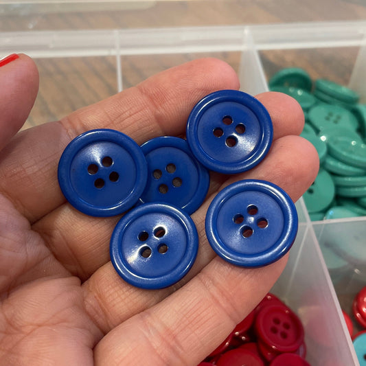 Hand holding blue buttons with a container of colorful buttons in the background