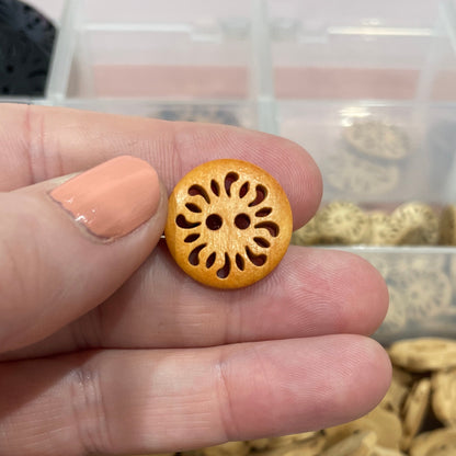 Hand holding a wooden button with a decorative center, against a background of various buttons in a clear container.