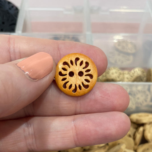 Hand holding a wooden button with a decorative center, against a background of various buttons in a clear container.