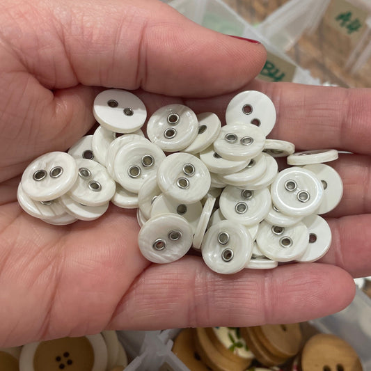 Hand holding a small pile of white buttons with a button collection container in the background.
