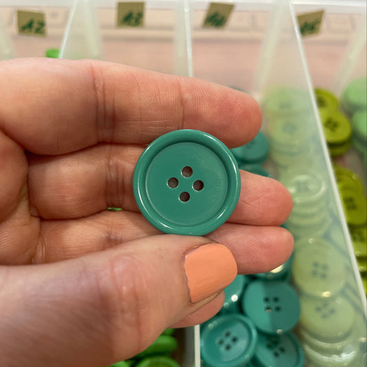 Hand holding a green button with a container of buttons in the background