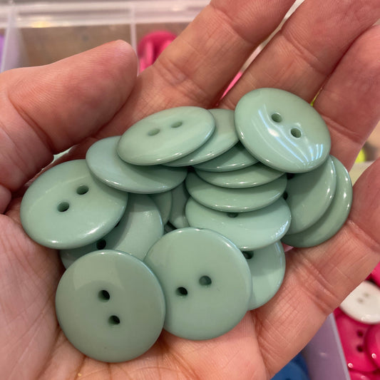 Hand holding light green buttons with a colorful button background