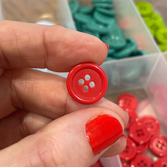 Red button held by a hand with a container of red buttons in the background