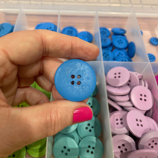 Hand holding a blue button with a container of colorful buttons in the background