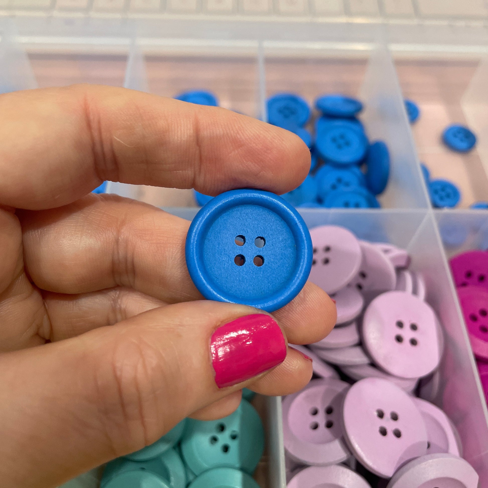 Hand holding a blue button with a container of colorful buttons in the background