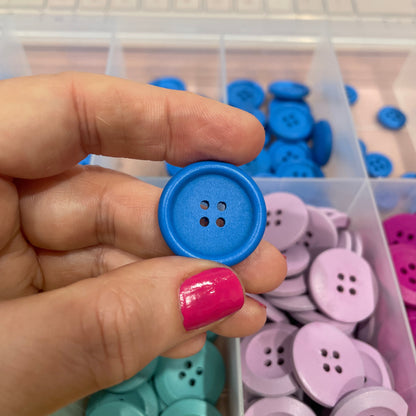 Hand holding a blue button with a container of colorful buttons in the background