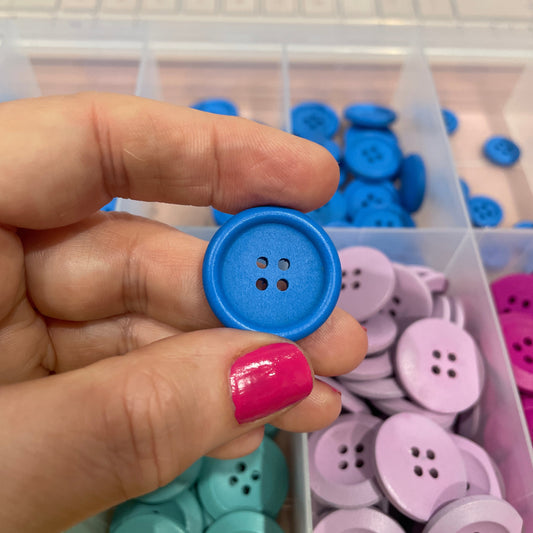 Hand holding a blue button with a container of colorful buttons in the background