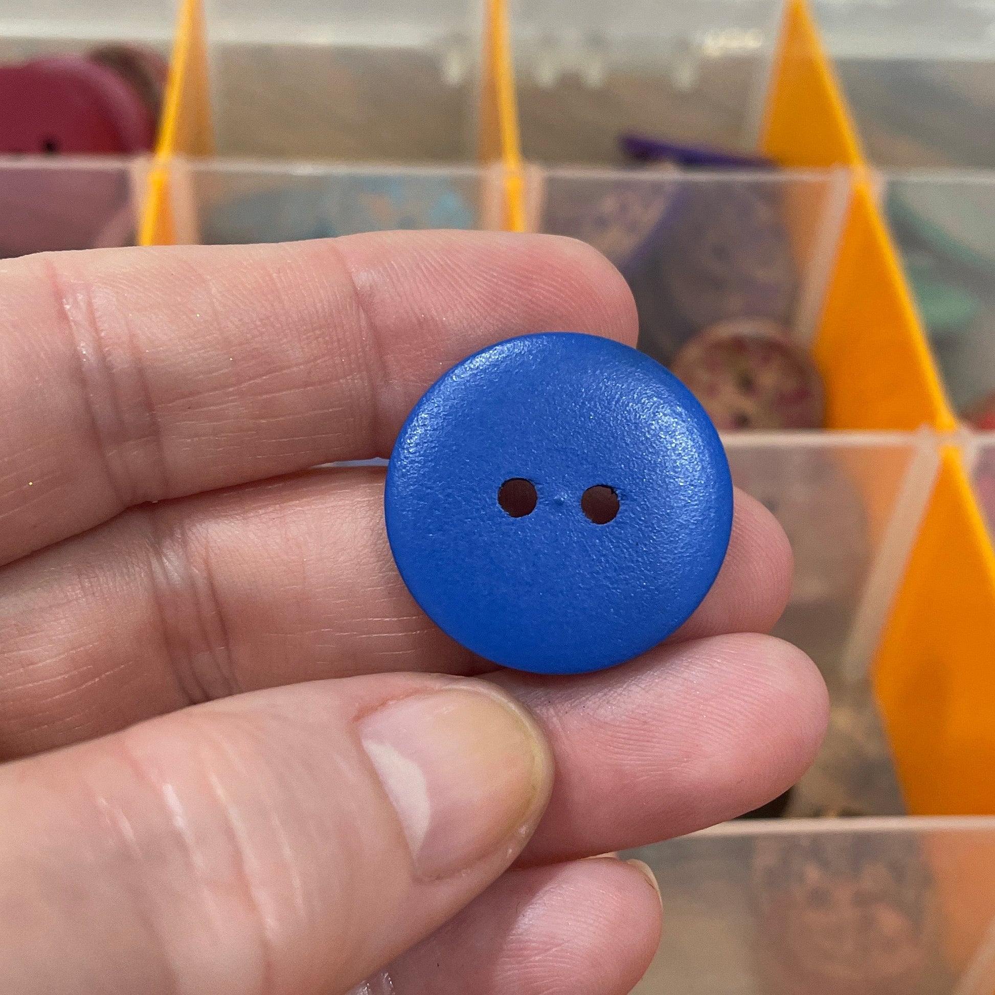 Hand holding a blue button with a background of colorful buttons in a case.
