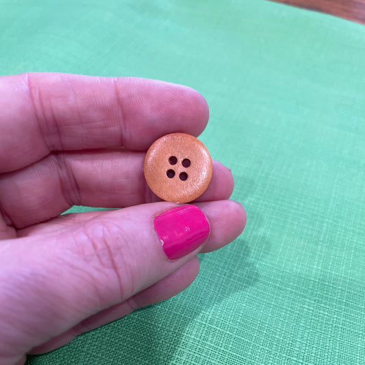 Hand holding a small round button with four holes against a green fabric background