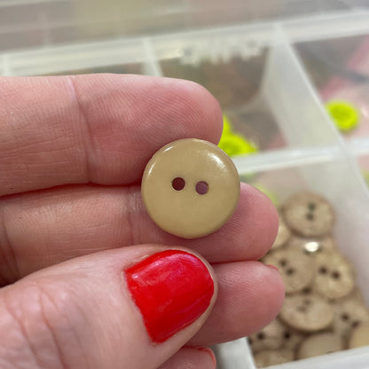 Hand holding a beige button with a container of various buttons in the background