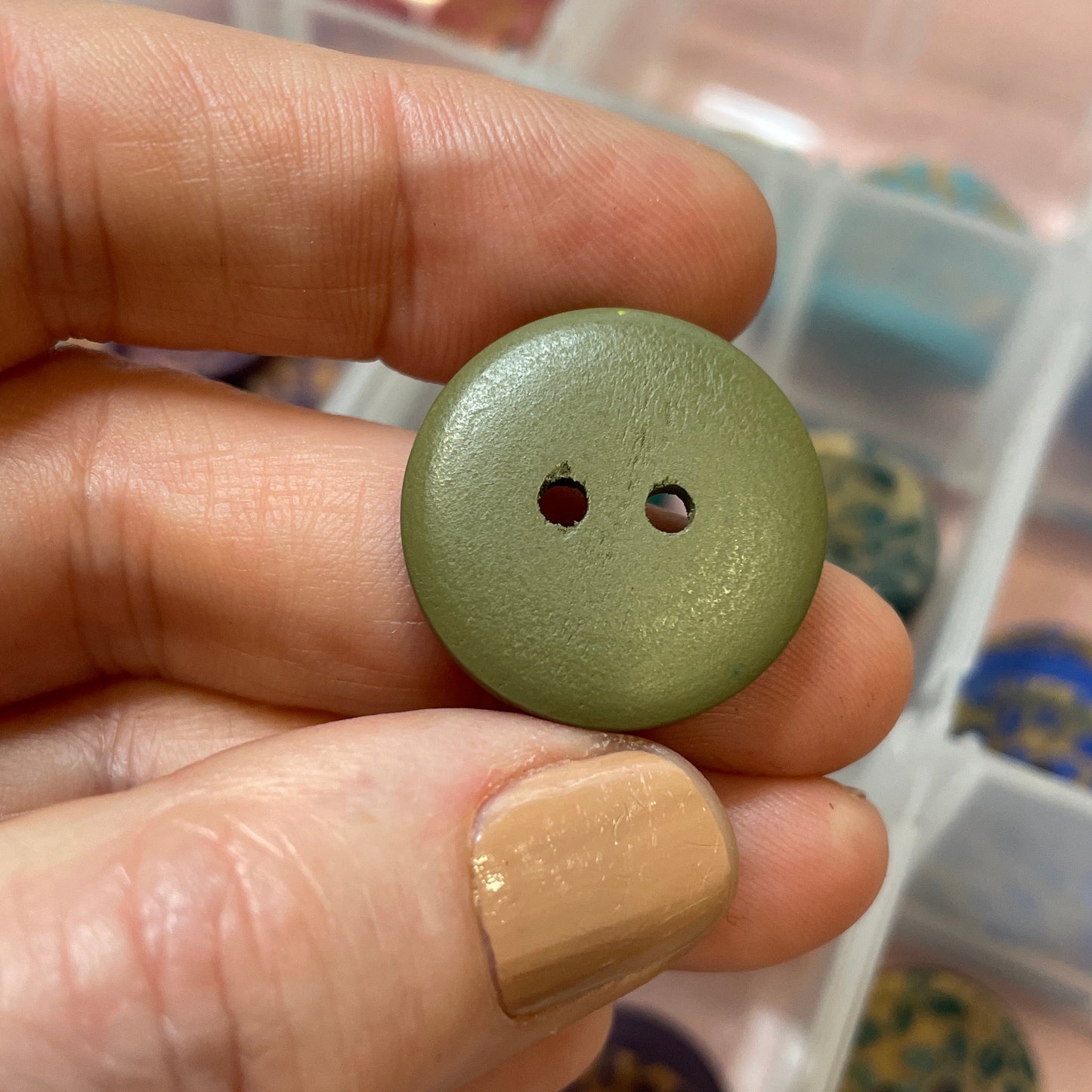 Hand holding a green button with a container of buttons in the background