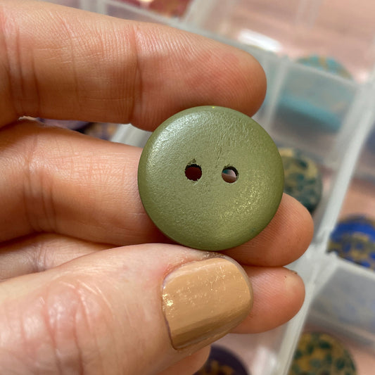 Hand holding a green button with a container of buttons in the background