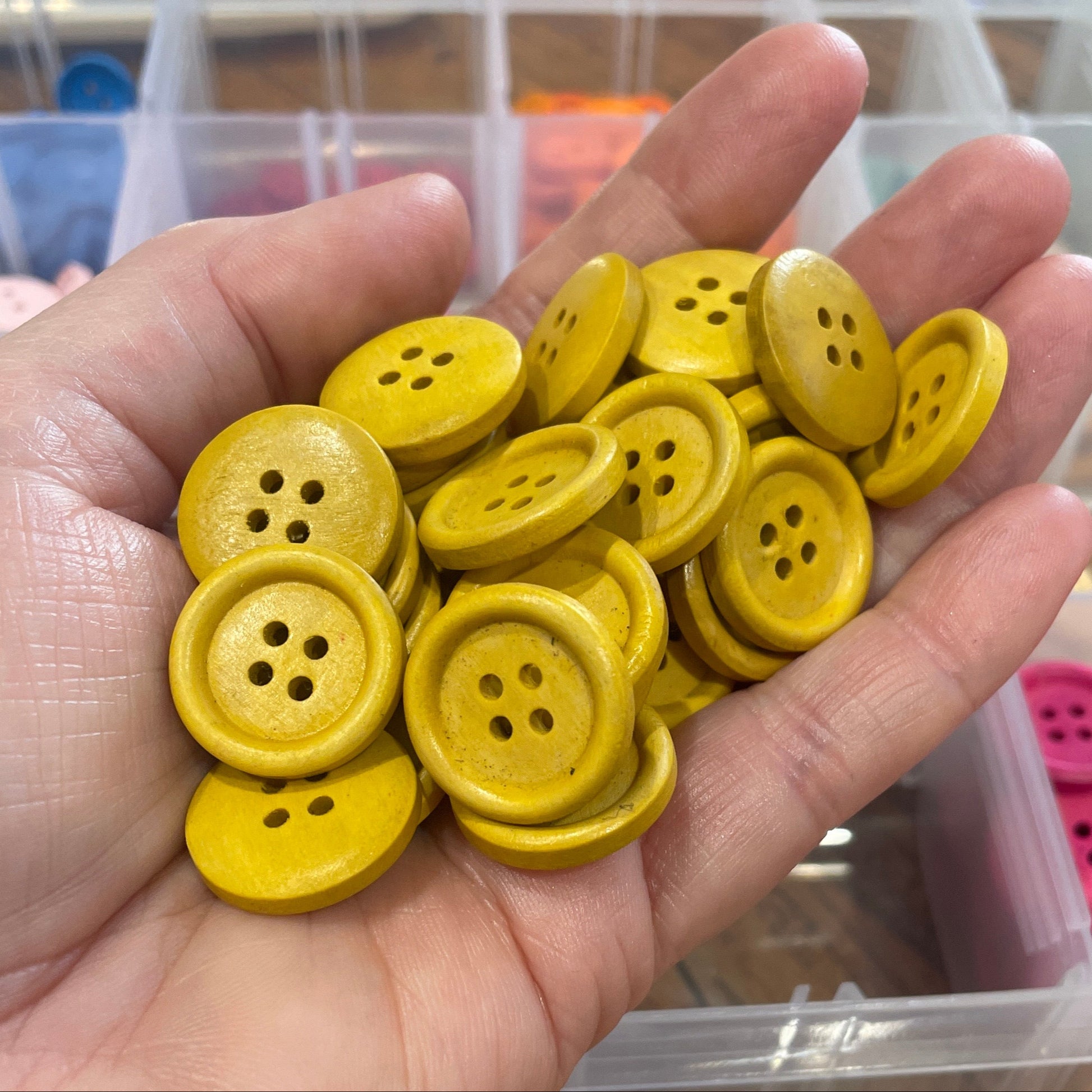 Hand holding yellow buttons with a container of buttons in the background