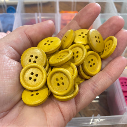 Hand holding yellow buttons with a container of buttons in the background