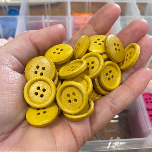 Hand holding yellow buttons with a container of buttons in the background