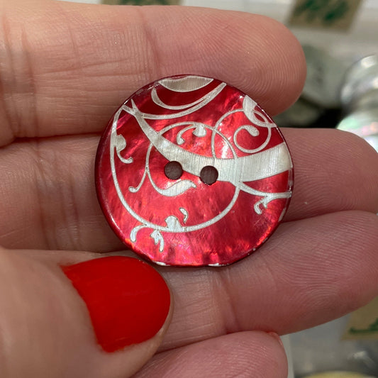 Red button with white patterns held between fingers against a blurred background of buttons