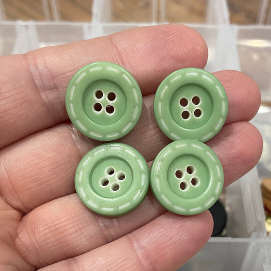 Hand holding green buttons with a container of assorted buttons in the background