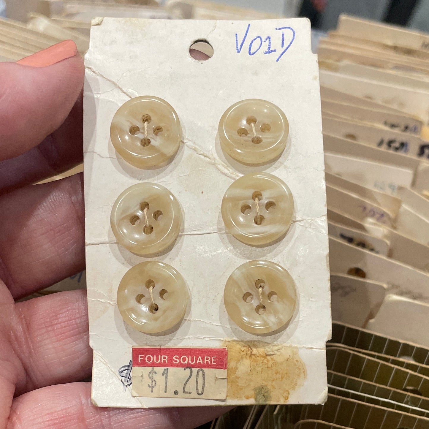 Hand holding a card with six beige buttons against a background of similar cards.