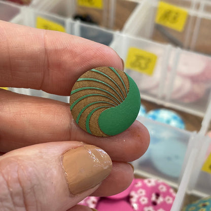 Hand holding a green button with a pattern, surrounded by various buttons in a container.