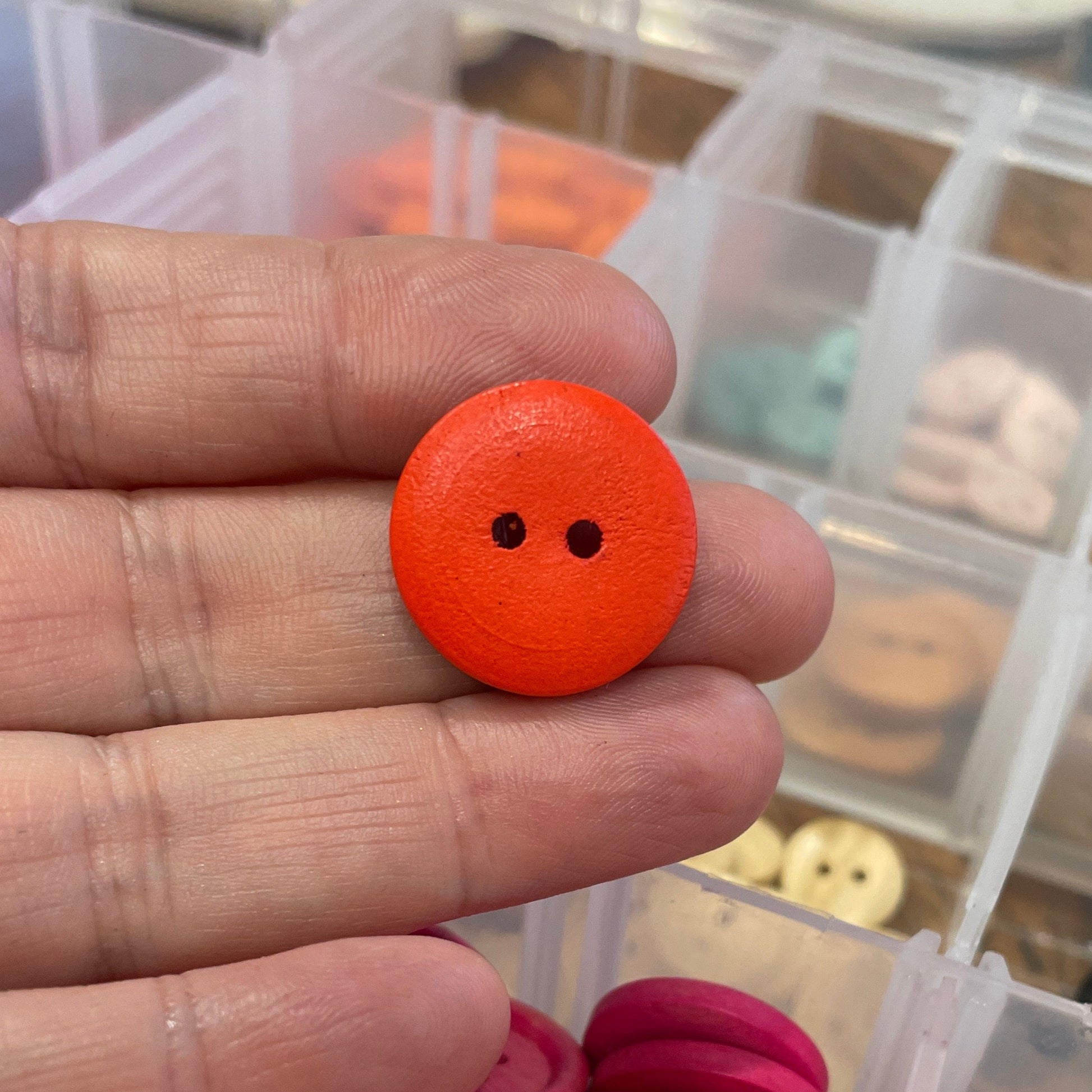 Hand holding an orange button with a container of buttons in the background