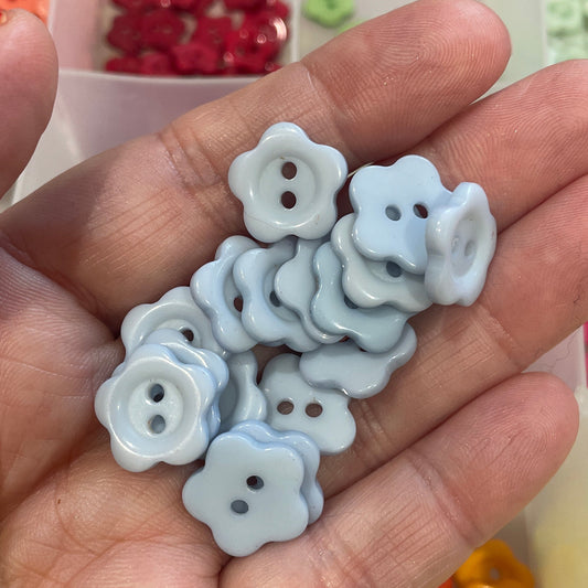Hand holding small white flower-shaped buttons with a background of colorful buttons.