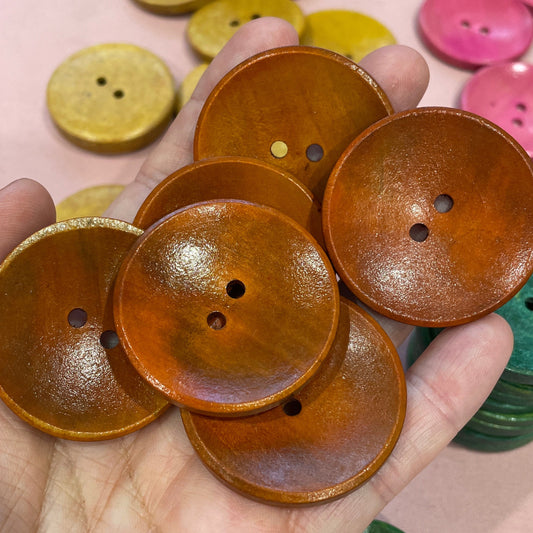 Hand holding brown buttons with colorful buttons in the background on a desk.
