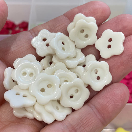 Hand holding white floral buttons with a blurred background of colorful buttons.